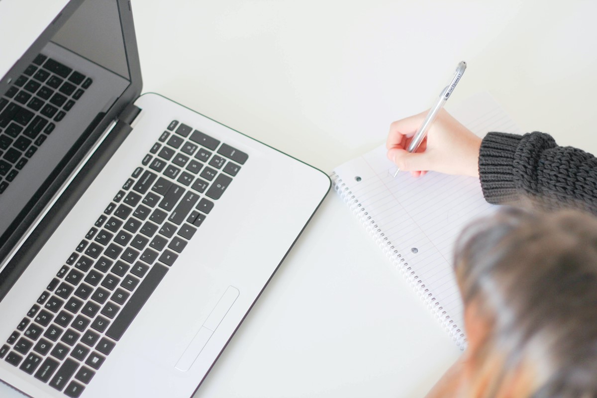 Person viewing a laptop while taking notes on paper